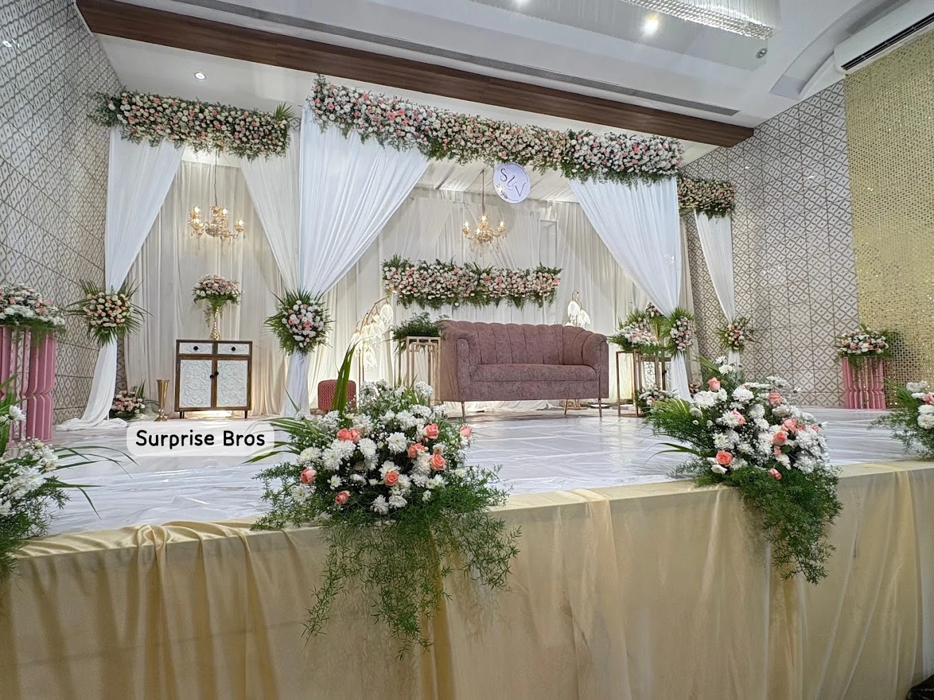White draped wedding stage with floral arrangements and a mauve sofa