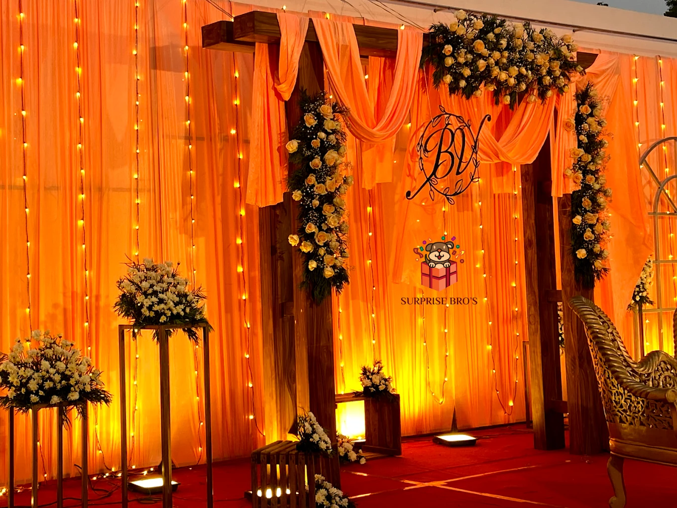 Amber-lit celebration stage with drapes, white flowers and string lights