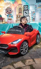 Small birthday photograph of a child in a red toy car